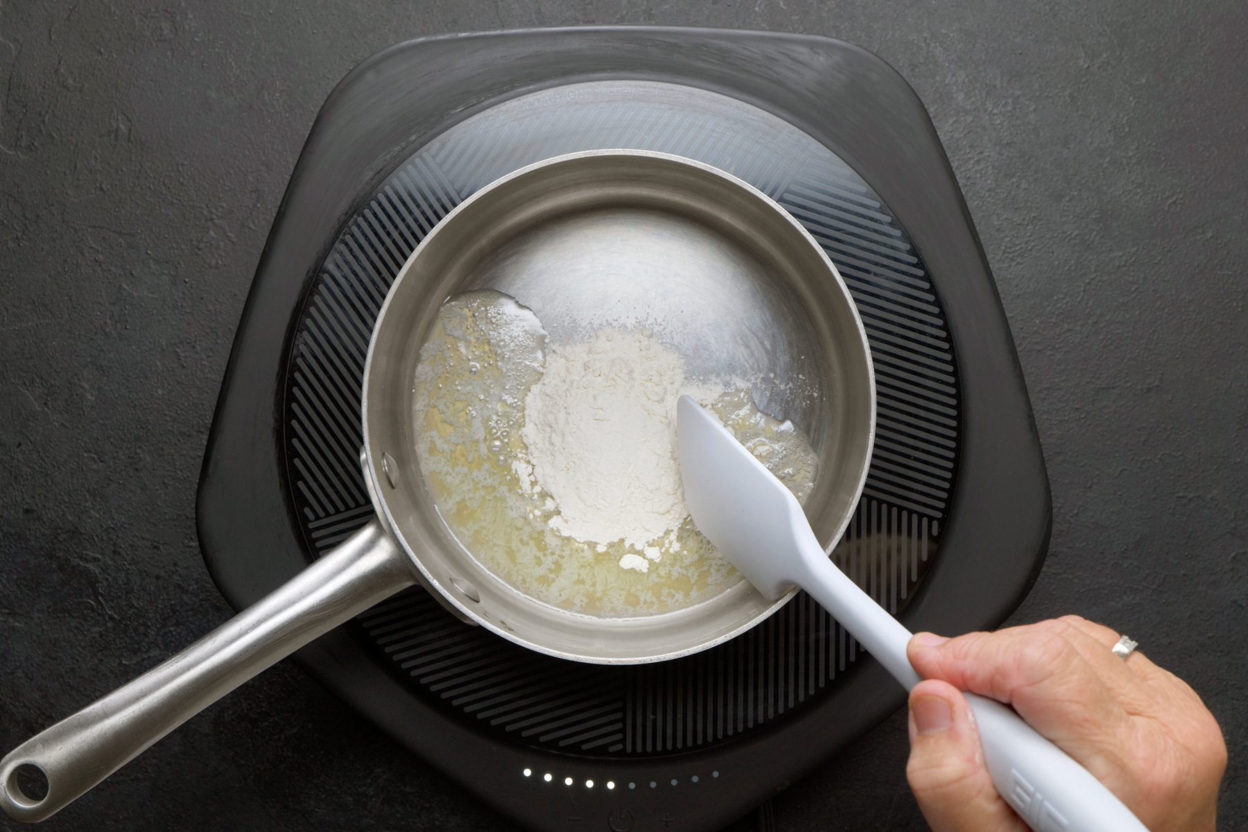 overhead shot of a small saucepan on an electric induction cooktop, The saucepan contains melted butter and a sprinkling of flour, The butter is a golden brown color, and the flour is a white powder, The mixture is starting to bubble and sizzle, indicating that it is heating up