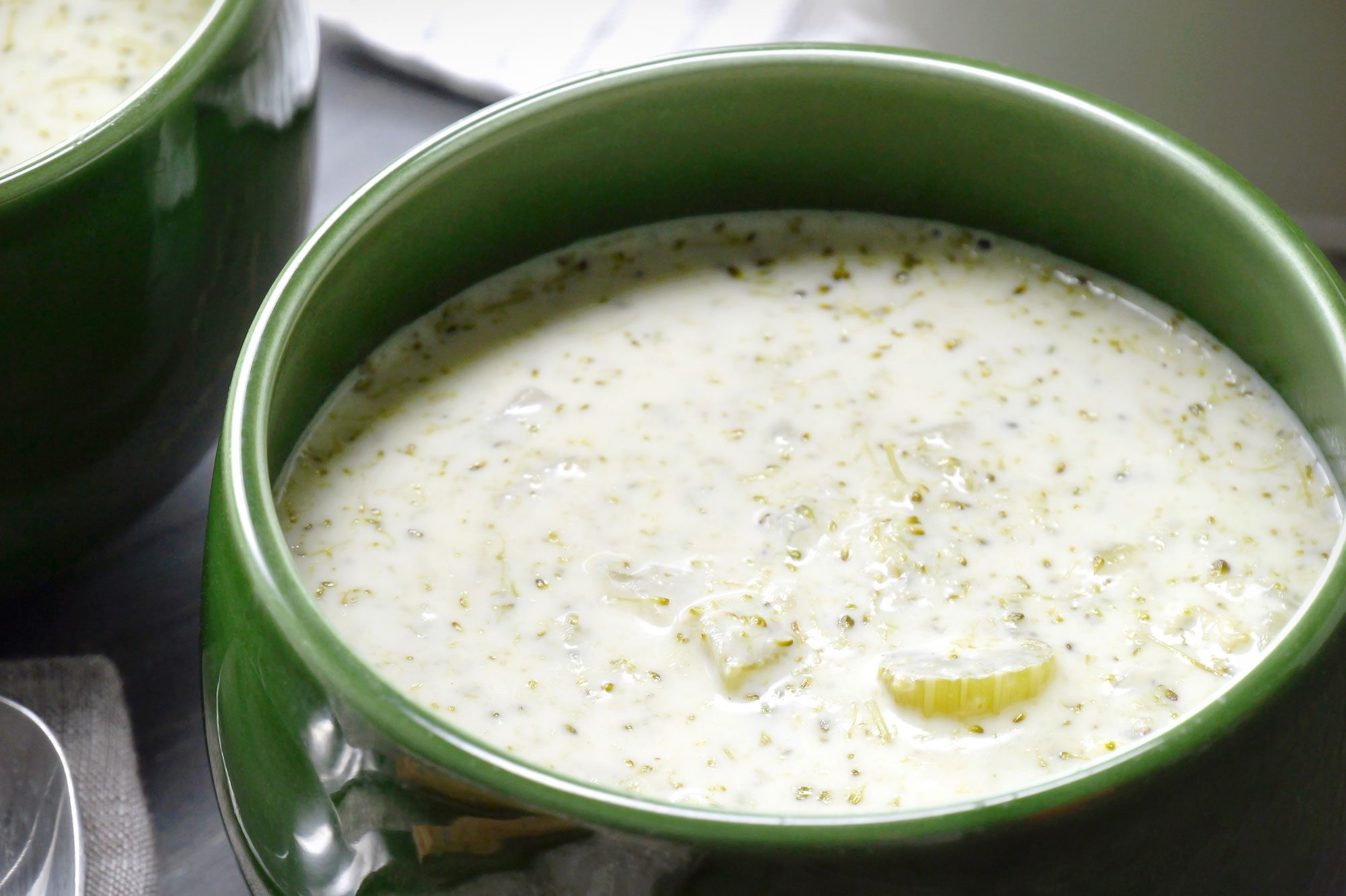 close shot of Two green bowls filled with Creamy Broccoli Soup are showcased, The soup is a creamy, pale yellow color with visible flecks of broccoli, The texture appears thick and smooth;
