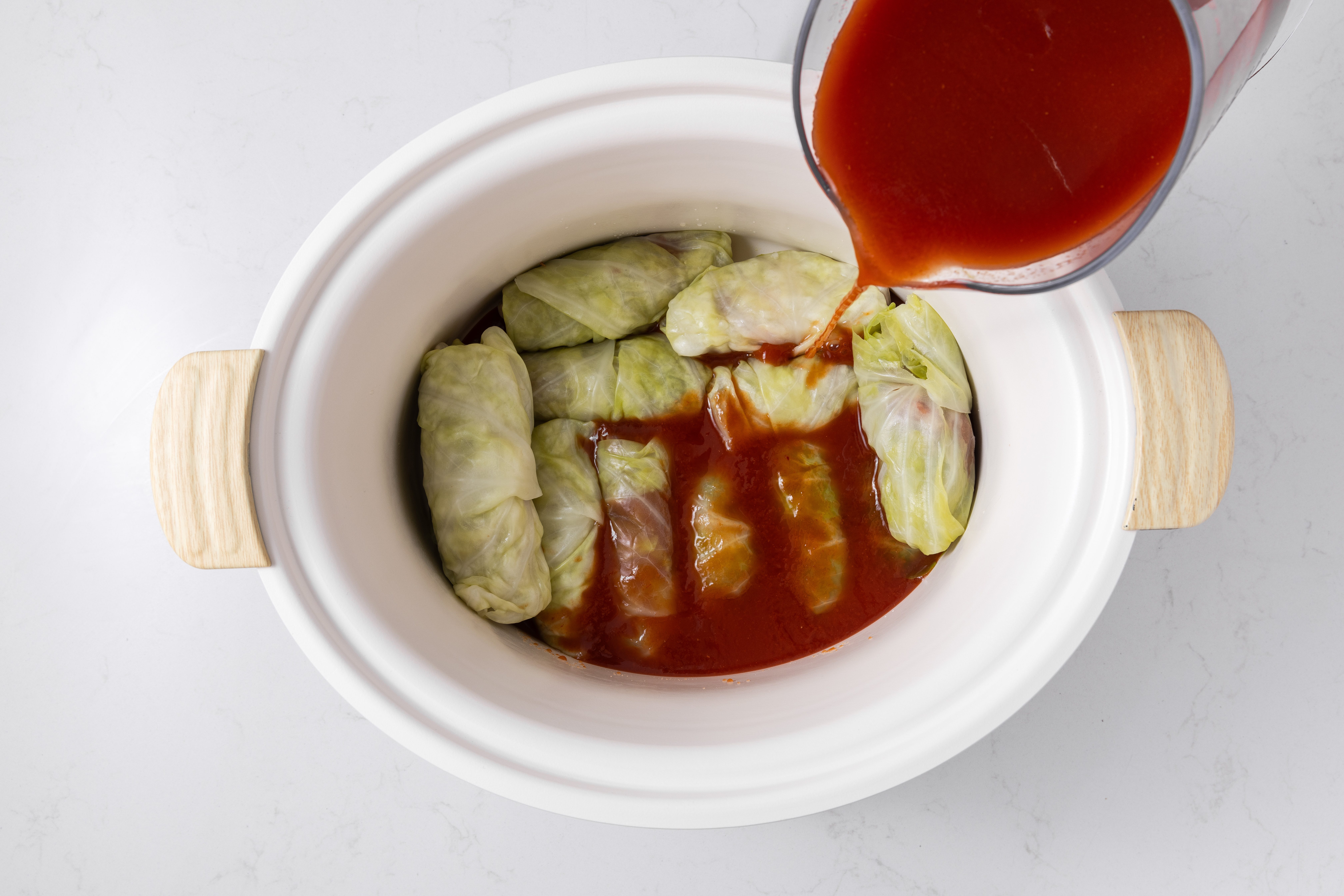 Cabbage rolls being added to the slow cooker with V8 juice to cook.