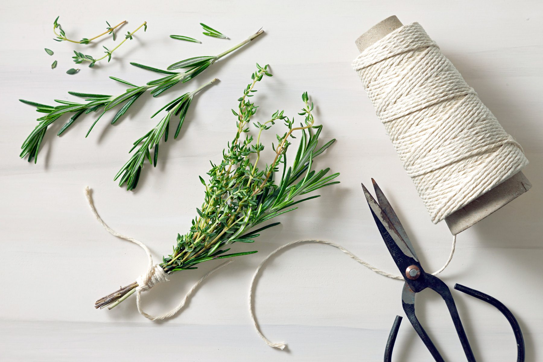 A bundle of thyme and rosemary sprigs is tied together at the root end with kitchen twine, then set aside for later use.
