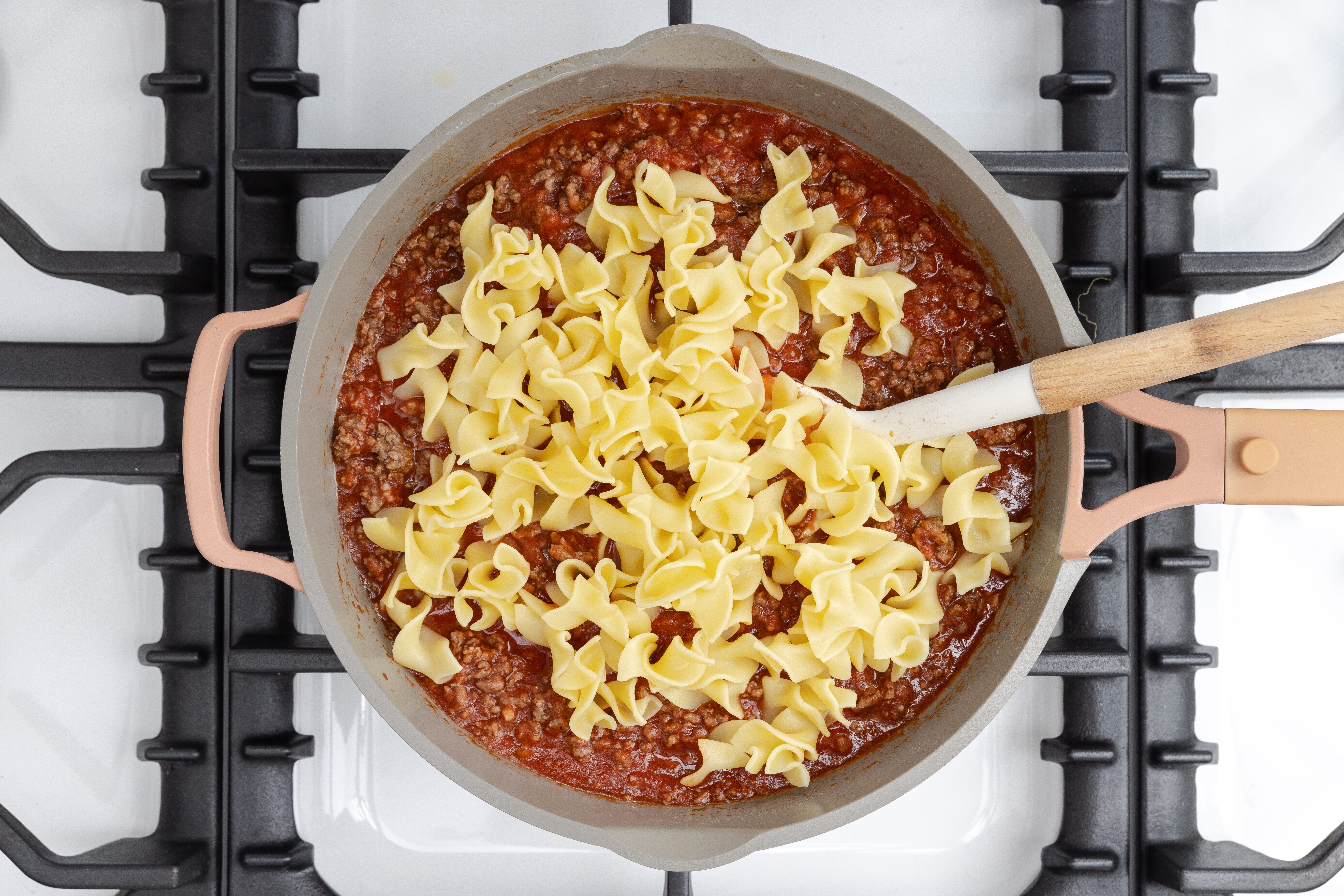 Beef mixture and noodles being combined in skillet.