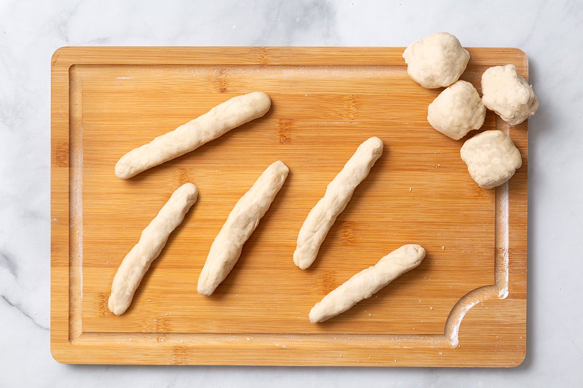 Bread dough shaped in 6-inch ropes on a wooden cutting board for step four of Homemade Breadsticks for Taste of Home