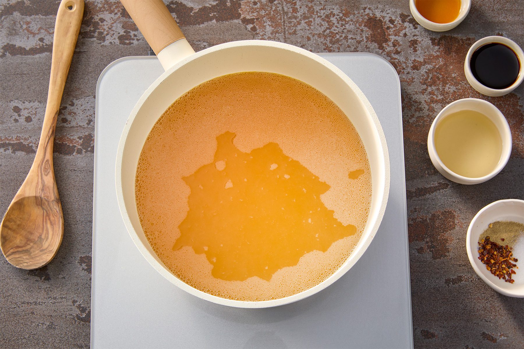 Overhead shot of a large saucepan or stock pot; bring chicken stock to a simmer; wooden spoon; brown texture background;