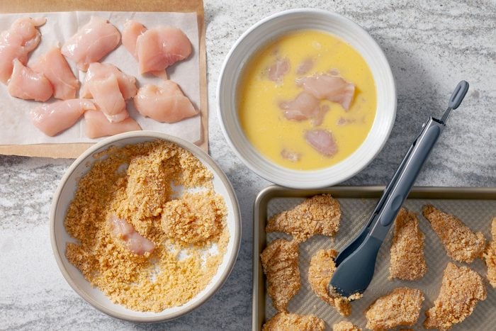 Chicken nuggets dipped in beaten eggs in one bowl. In another bowl they are dredged in keto breading mixture.