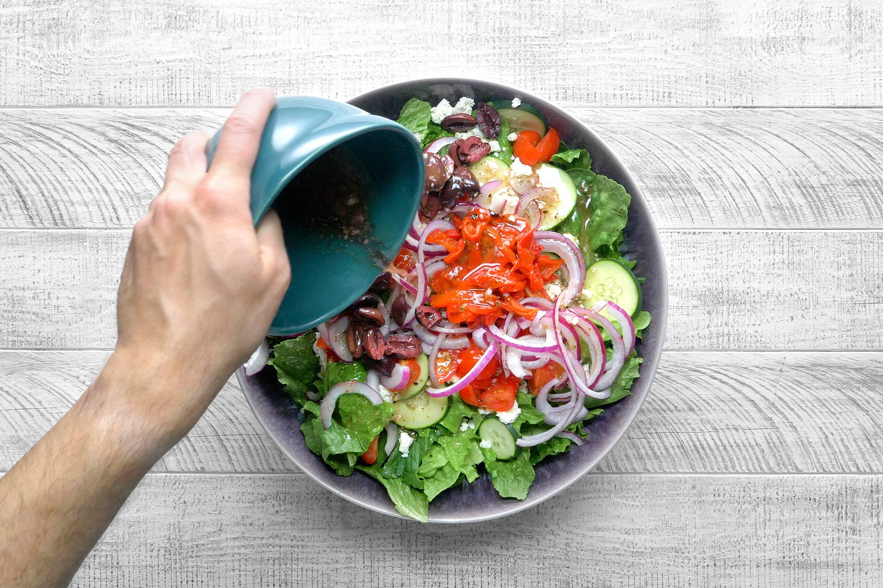 Overhead shot of drizzle dressing mixture over salad and toss to coat; grey wooden surface;