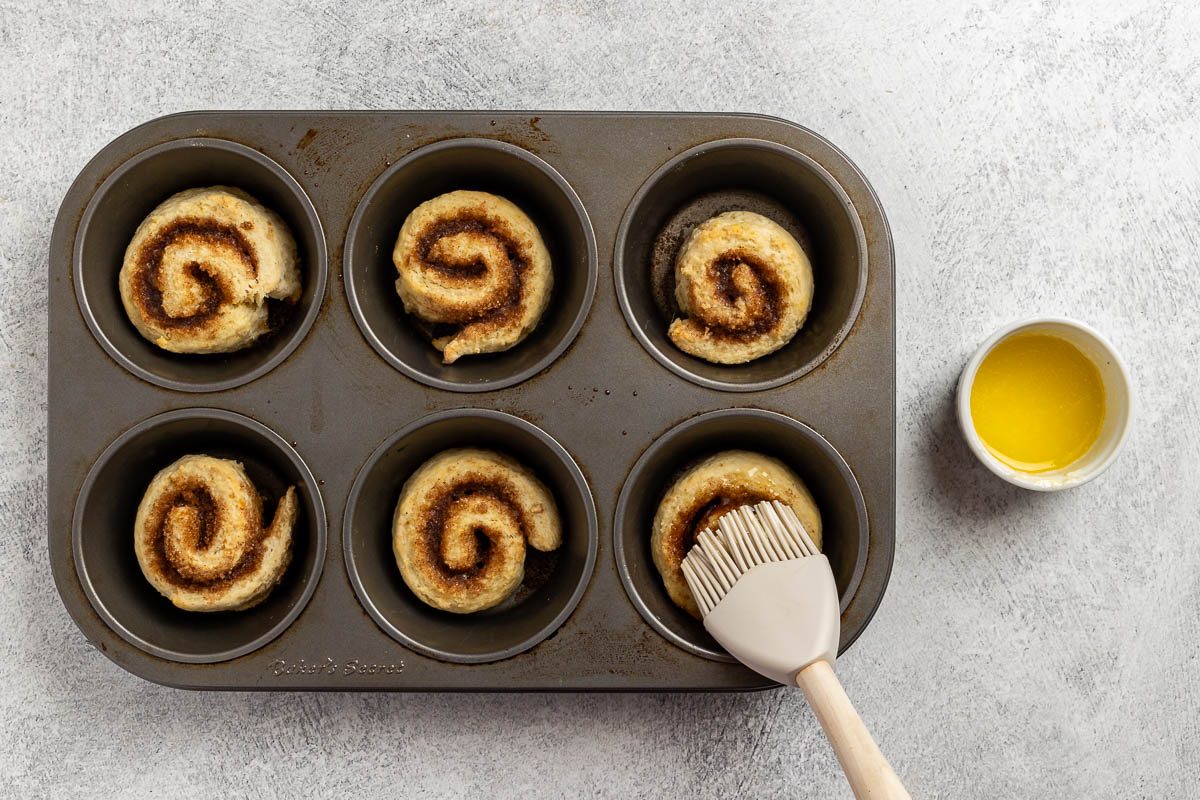 baked cinnamon rolls in a muffin tin brushed with butter.
