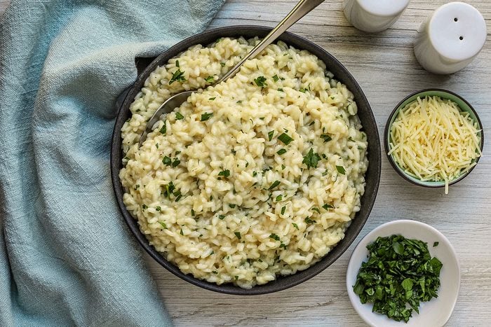 A serving of Parmesan risotto with extra parsley and shredded Parmesan cheese.