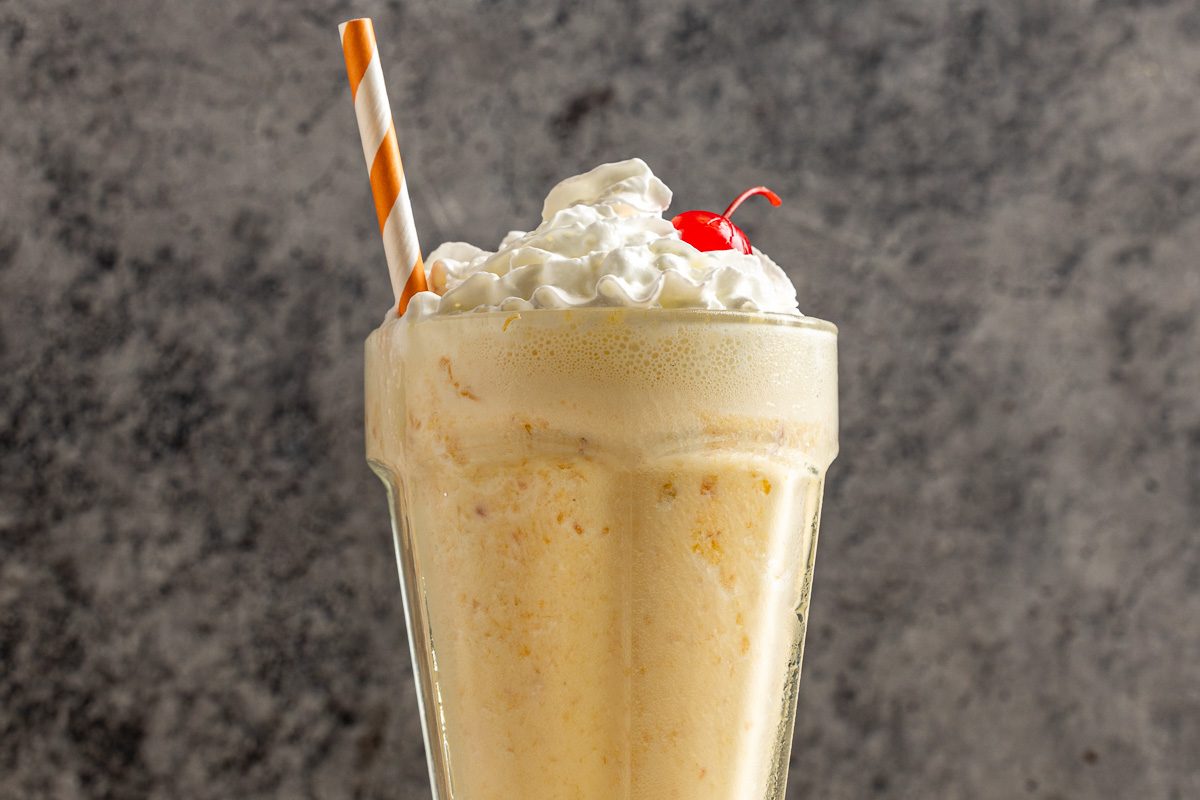 Taste of Home Peach Milkshake photo of the finished recipe topped with whipped cream and a cherry.