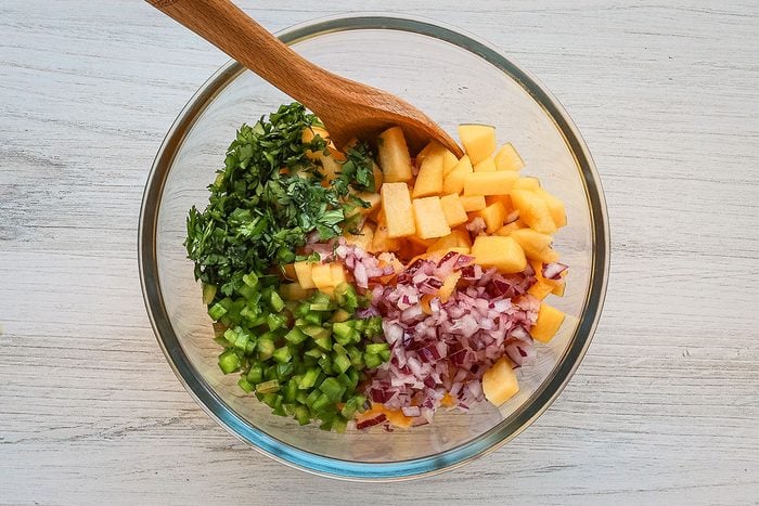 Combining the ingredients for a fruity peach salsa with cilantro, jalapeno pepper, lime juice and red onion.