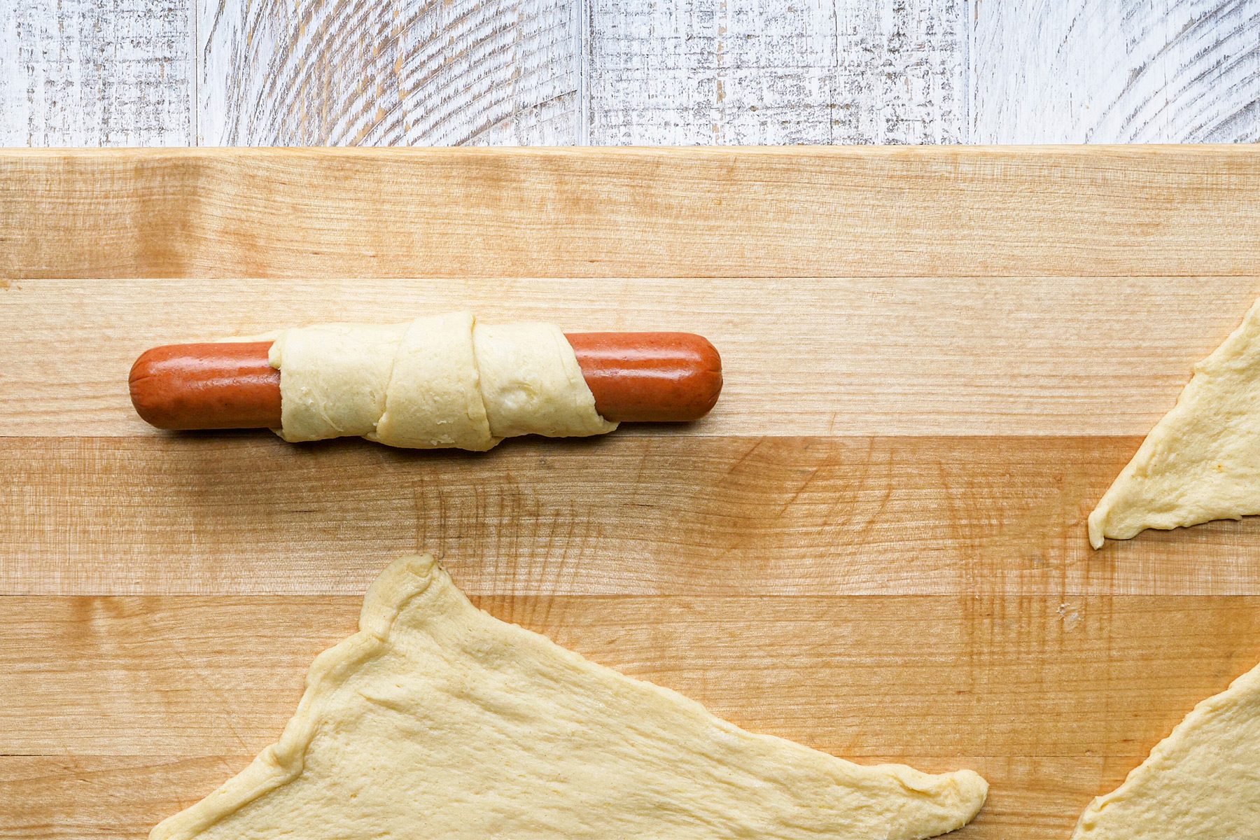 overhead shot; white wooden textured background; hot dogs; at wide ends; of triangles and rolled up; over wooden board;