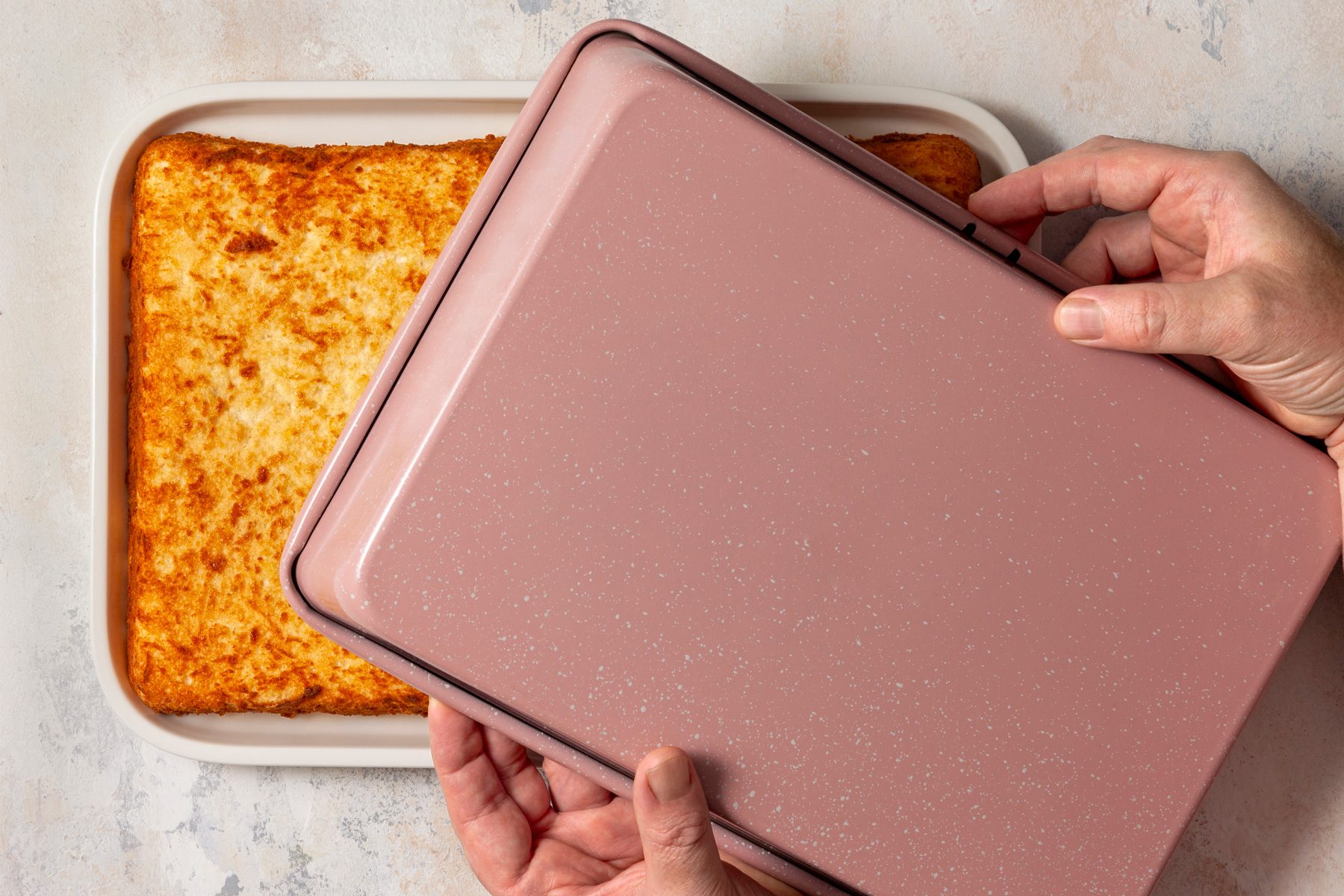 The baked cake is being flipped onto a platter, showcasing its golden-brown top.