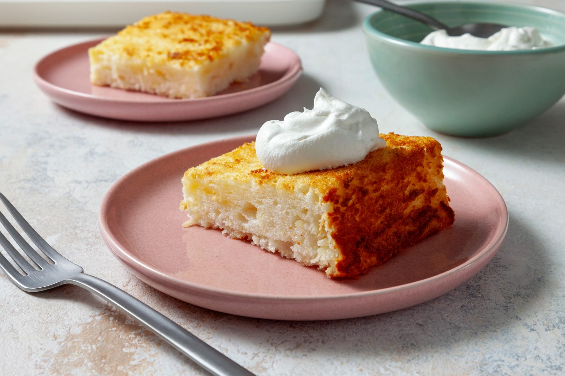 A three-quarter shot captures a slice of Pineapple Angel Food Cake, elegantly topped with whipped cream. The light, airy texture of the cake is visible, along with the pineapple pieces adding a pop of color.