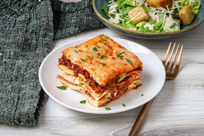 Pizza Lasagna on a plate with a Caesar salad in the background.