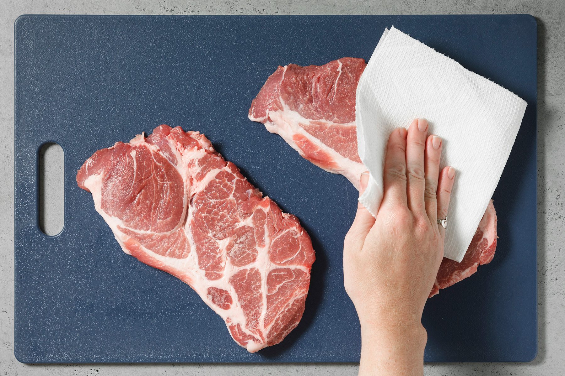 Steaks are patted dry with a paper towel.