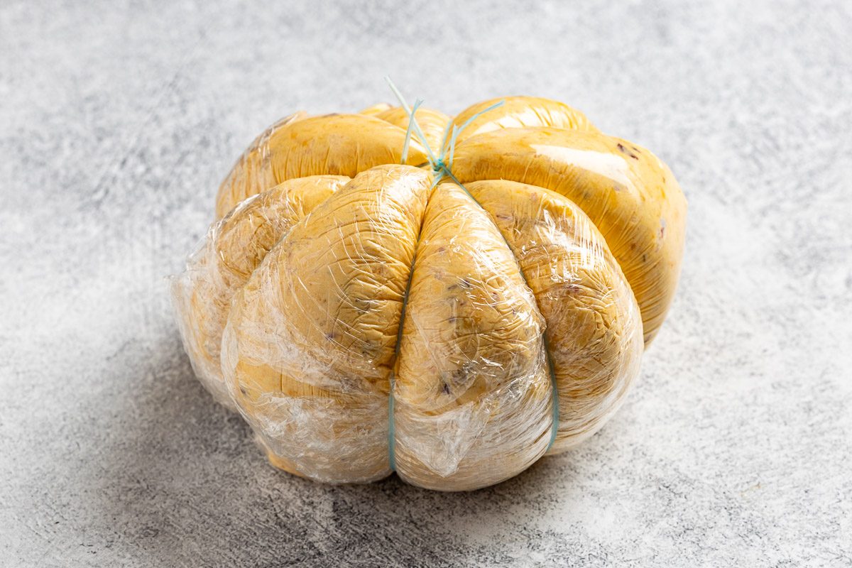 Taste of Home Pumpkin Cheese Ball photo of the cheese ball wrapped in four pieces of string (or four rubber bands), creating indentions to resemble a pumpkin
