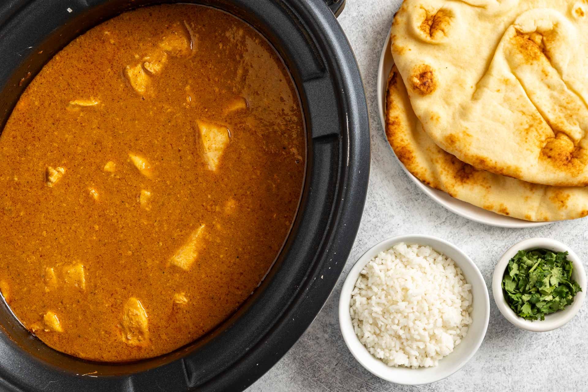 cooked butter chicken with rice, cilantro and naan bread.