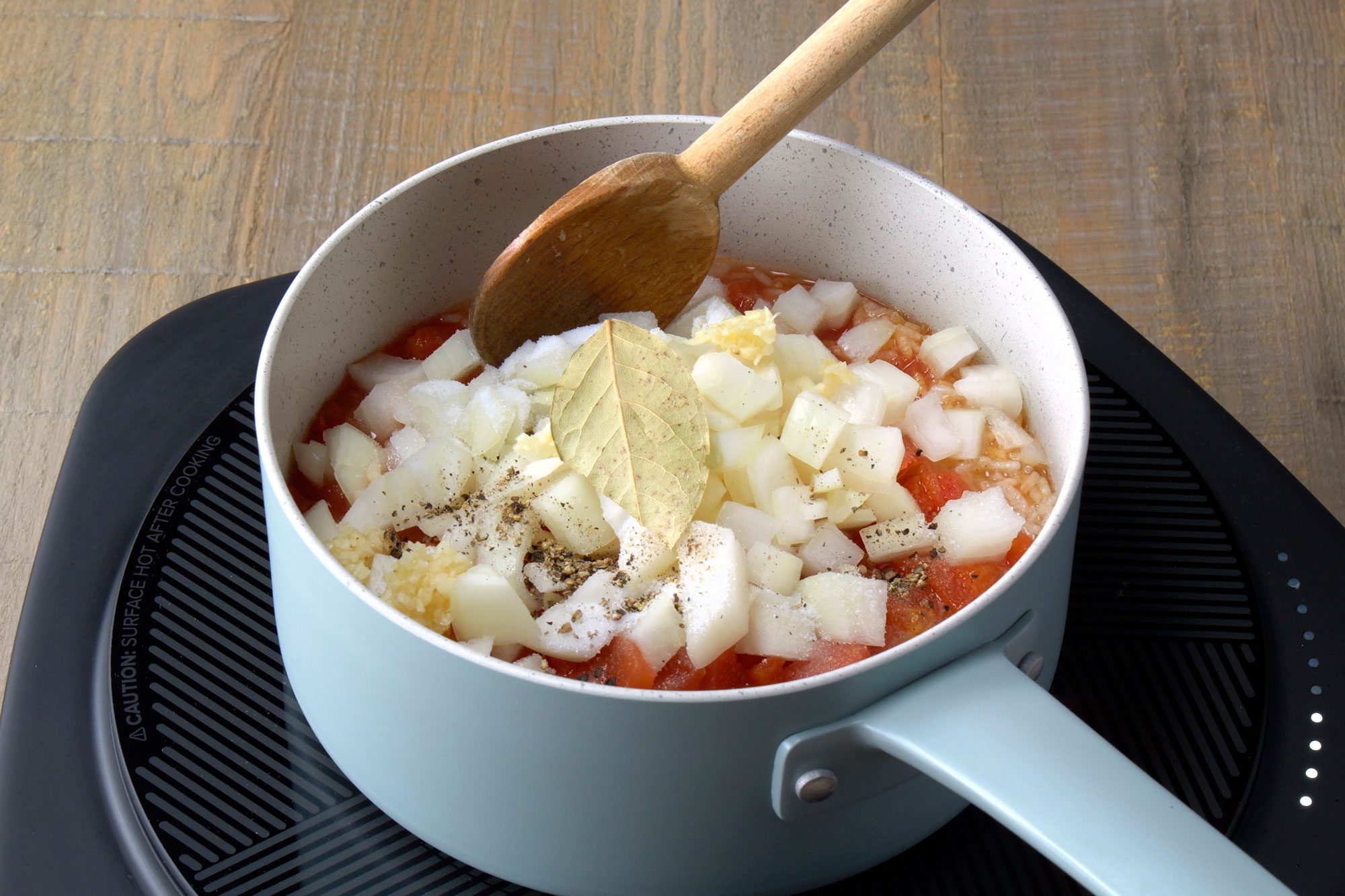 The saucepan contains a mixture of chopped onions, chopped tomatoes, and a bay leaf