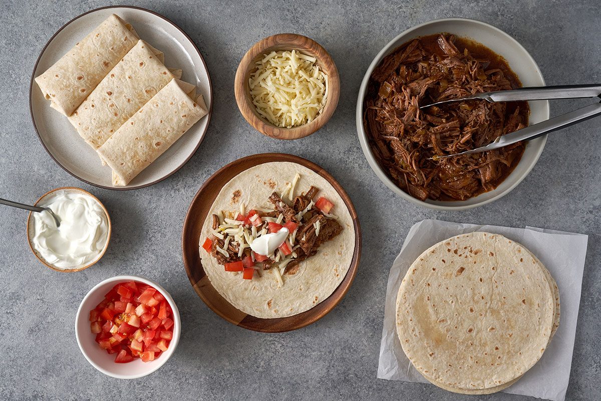 Spoon the shredded beef into the center of each tortilla, top with cheese, tomatoes, and sour cream, then fold up the burritos for a perfect Shredded Steak Burritos recipe.