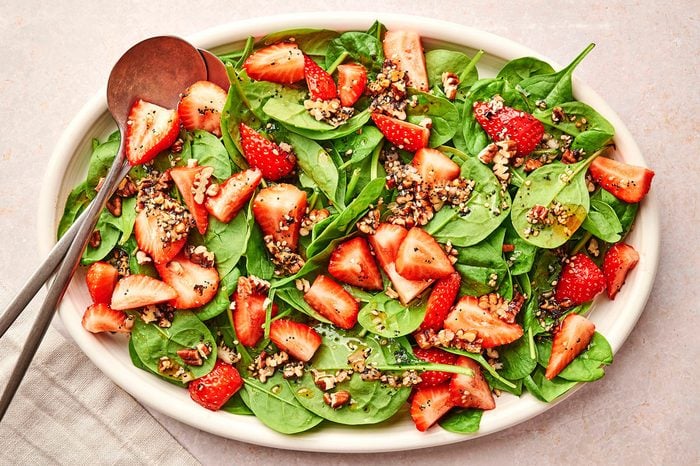 A white serving platter with the strawberry spinach salad recipe by Taste of Home, with two metal serving spoons