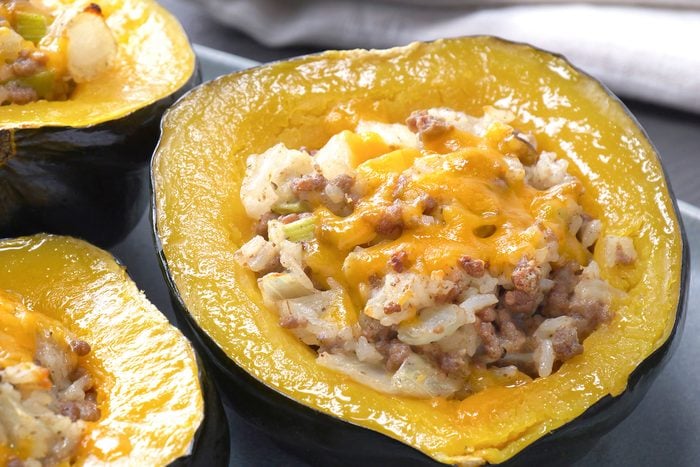 a close-up of stuffed acorn squash halves, The squash shells are a vibrant orange color, while the filling is a mixture of ground meat (likely beef or sausage), rice, vegetables, and melted cheese, The filling is a golden brown color and is topped with a layer of shredded cheddar cheese;