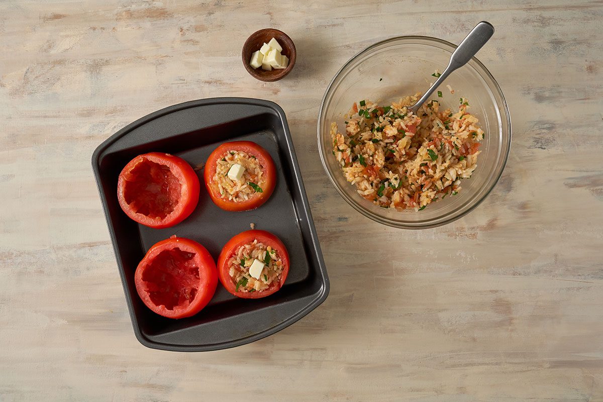 The rice mixture being stuffed into the hollowed-out tomatoes, and dotted with butter on top for the Stuffed Tomatoes with Rice recipe, by Taste of Home.