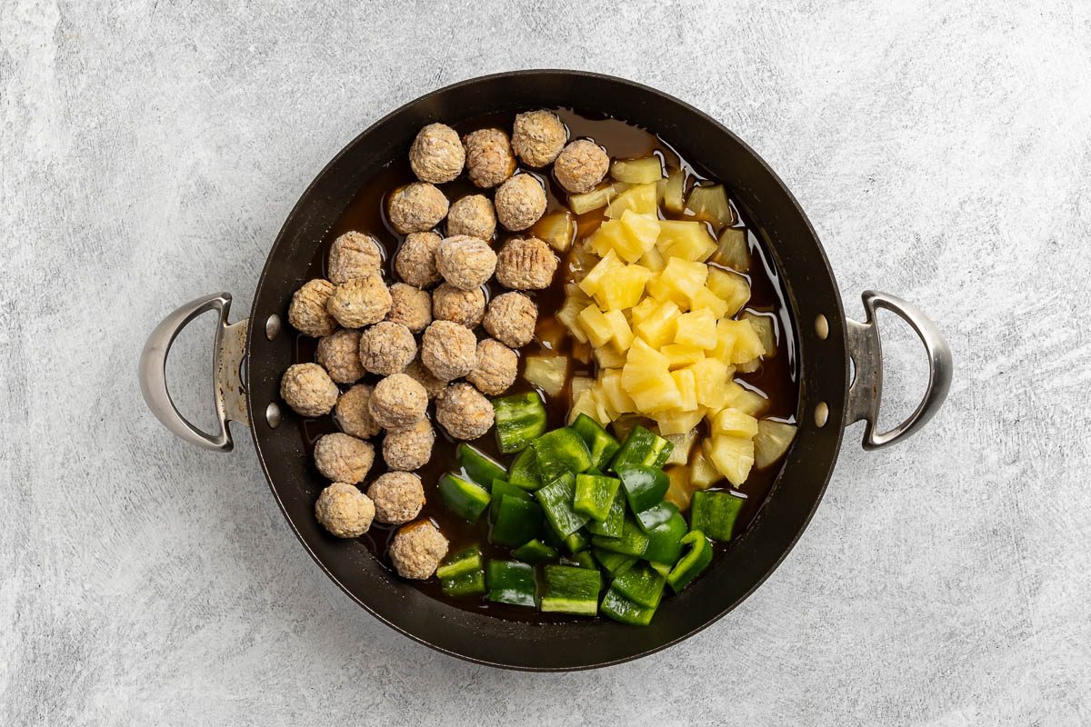 adding pineapple chunks, meatballs and green pepper to the sauce