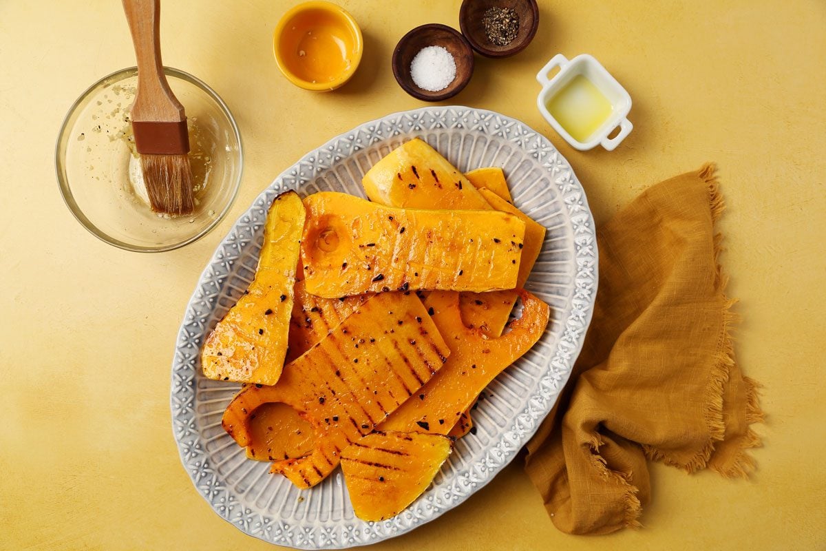 Process of making Taste of Home's Grilled Squash grilled butternut squash on a platter on a bright yellow surface.