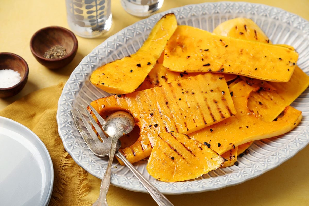 Close up of Taste of Home's Grilled Squash grilled butternut squash on a platter on a bright yellow surface.