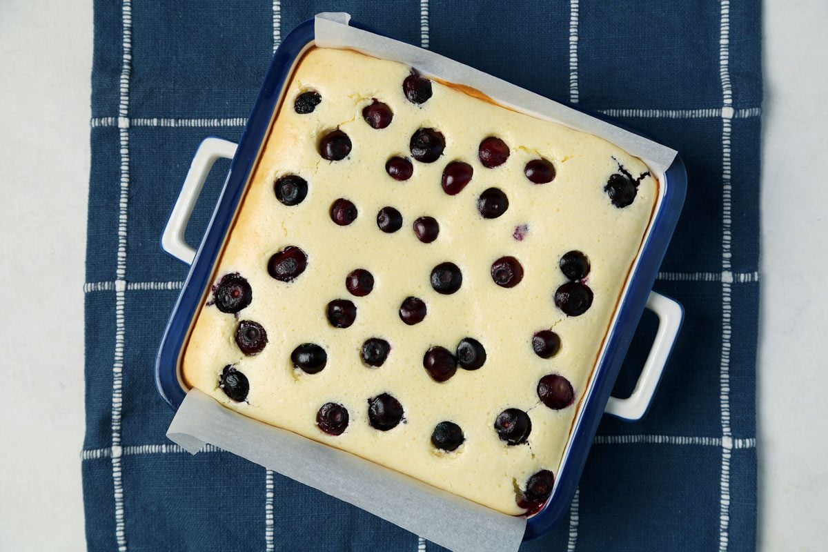Process of making Taste of Home's Blueberry Cheesecake Bars in a baking dish on a blue linen cloth.