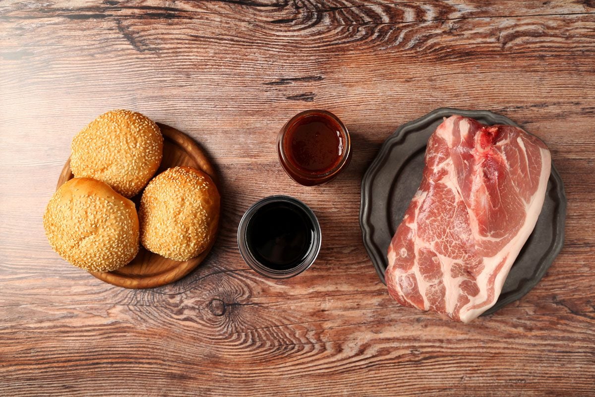 Ingredients for Taste of Home's Root Beer Pulled Pork laid out in small bowls on a brown wooden surface.