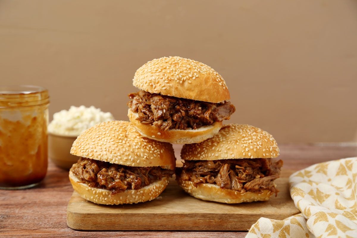 Close up of Taste of Home's Root Beer Pulled Pork assembled and on a wooden board on a dark brown wooden surface.