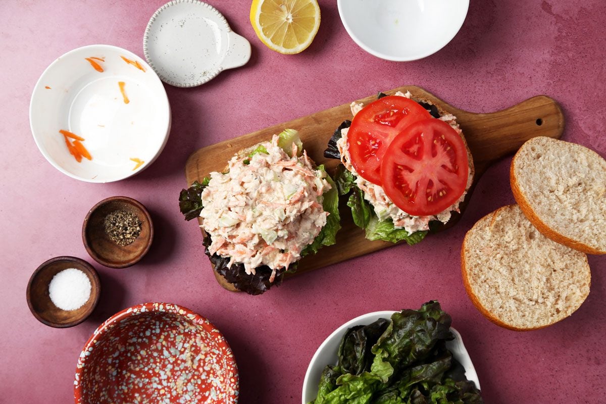 Process of making Taste of Home's salmon salad sandwich. Assembling sandwich on a small wooden board on a magenta surface.