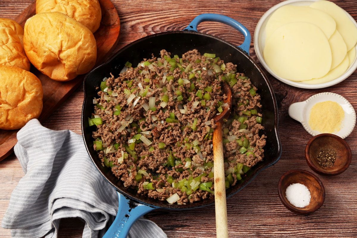 Process of making Taste of Home's Philly Cheesesteak Sloppy Joes on a brown wooden surface. Meat browned in a skillet.