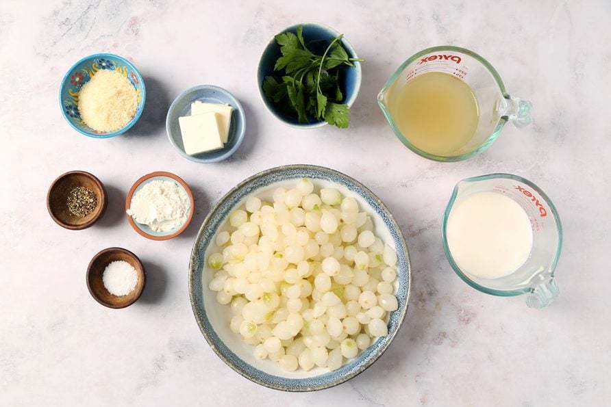 Ingredients for Taste of Home's Creamed Pearl Onions laid out in small bowls on a grey marble surface.