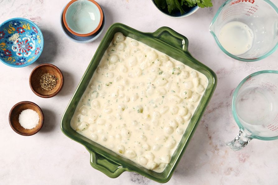 Process of making Taste of Home's Creamed Pearl Onions in a green casserole dish on a grey marble surface.
