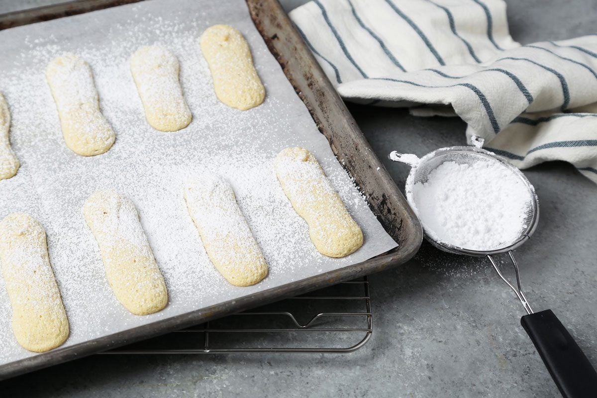 Close up of Taste of Home's Lady Fingers on a wire rack on a grey marble surface with powdered sugar.