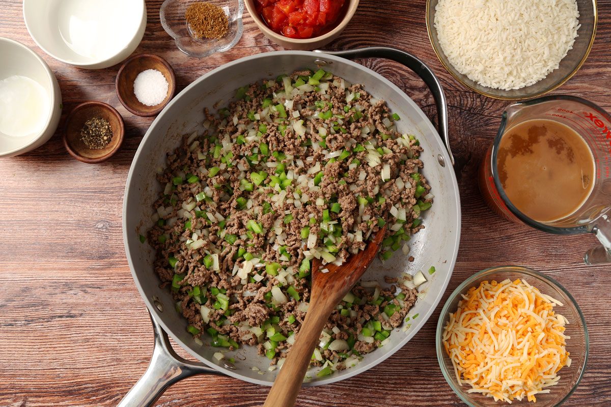 Process of making Taste of Home's Beef and Rice Skillet in a large skilet on a brown wooden surface.