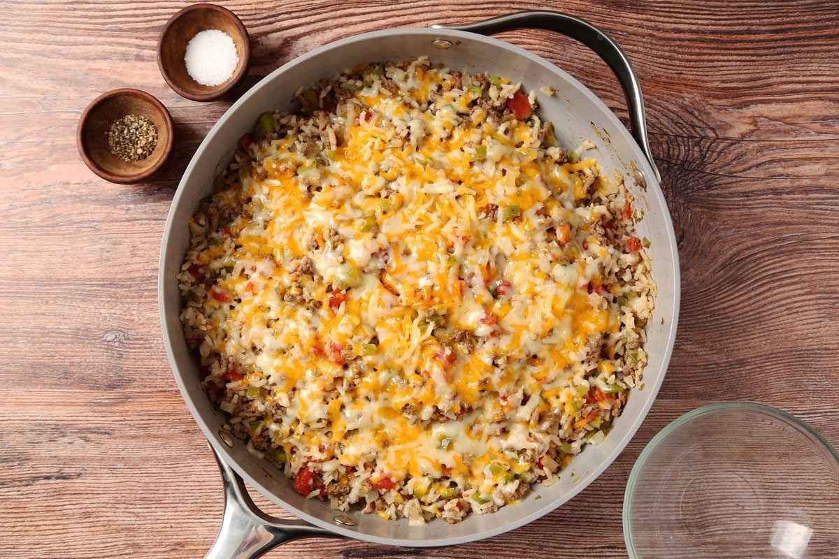 Process of making Taste of Home's Beef and Rice Skillet in a large skillet on a brown wooden surface.