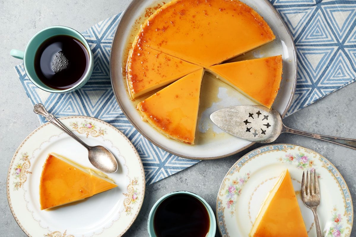 Close up of Taste of Home's Flan de Queso cut and served on plates on a grey surface.
