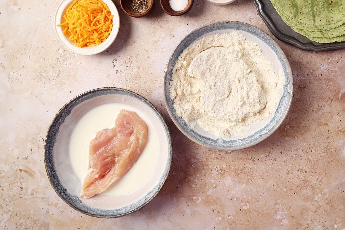 Process of making Taste of Home's Buffalo Chicken Wrap. Chicken being dredged in a bowl of flour and buttermilk.