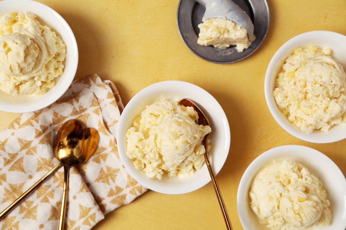 Close up of Taste of Home's Corn Ice Cream scooped and served in small white bowls on a yellow surface.