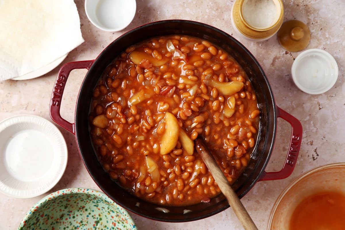 Process of making Taste of Home's Apple Pie Baked Beans in a large pot on a brown marble surface.