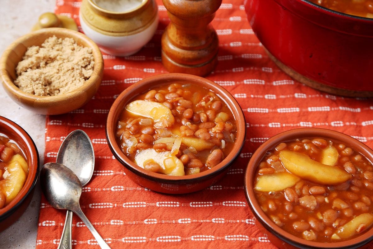 Close up of Taste of Home's Apple Pie Baked Beans served in small brown dishes on an orange towel on a brown marble surface.