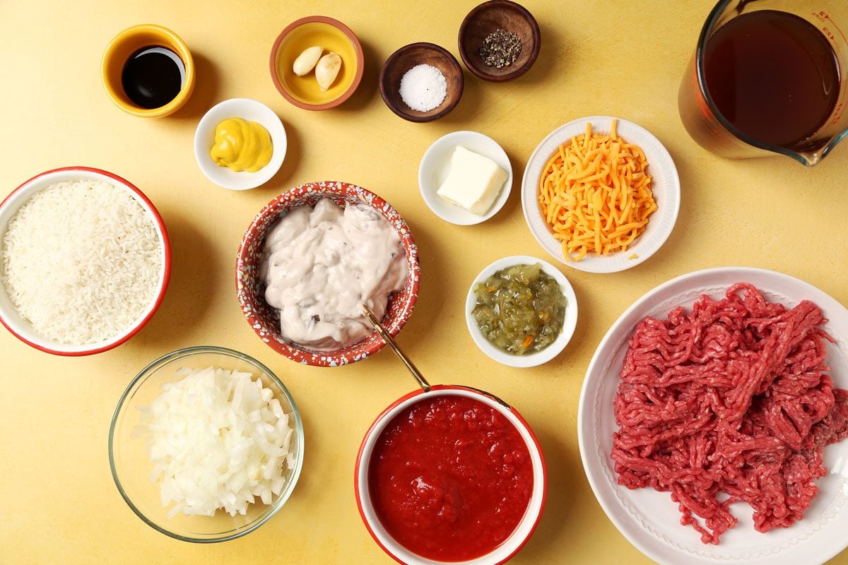 Ingredients for Taste of Home's Hamburger Casserole laid out in small bowls on a bright yellow surface.