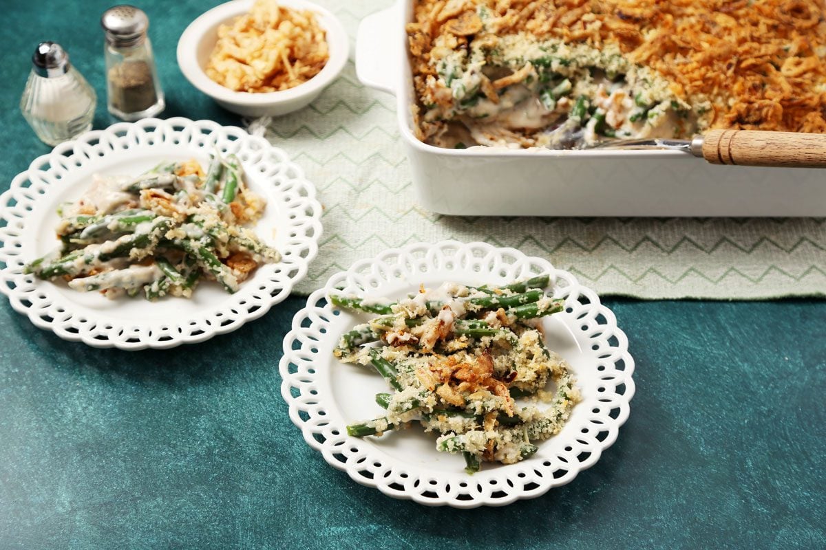 Close up of Taste of Home's Gluten Free Green Bean Casserole served on white lace plates on a teal surface.