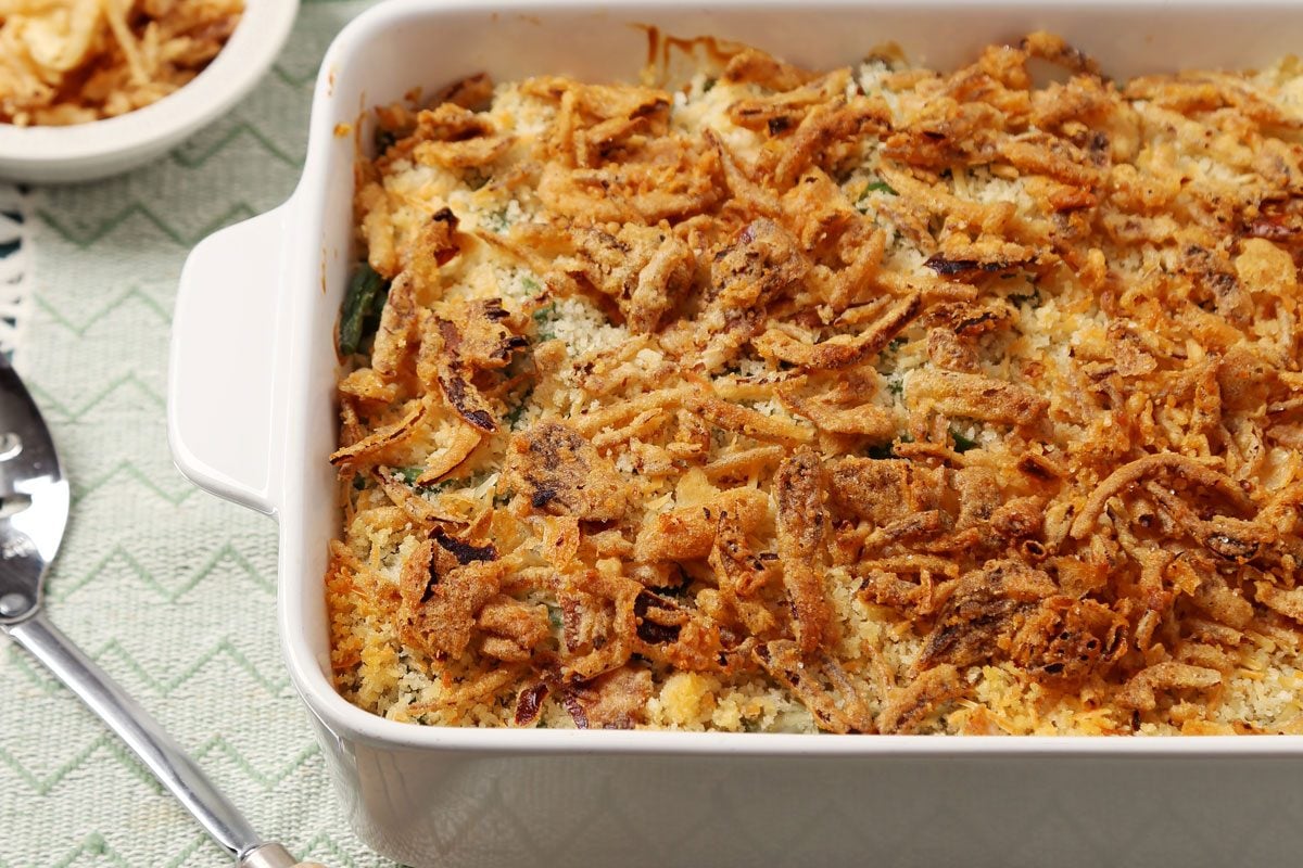 Close up of Taste of Home's Gluten Free Green Bean Casserole served on white lace plates on a teal surface.
