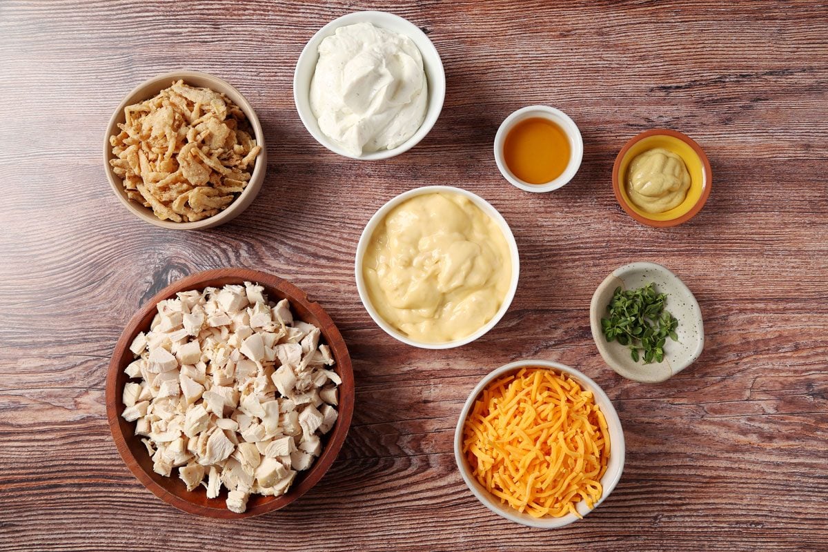 Ingredients for Taste of Home's French Onion Chicken Casserole laid out in small bowls on a brown wooden surface.