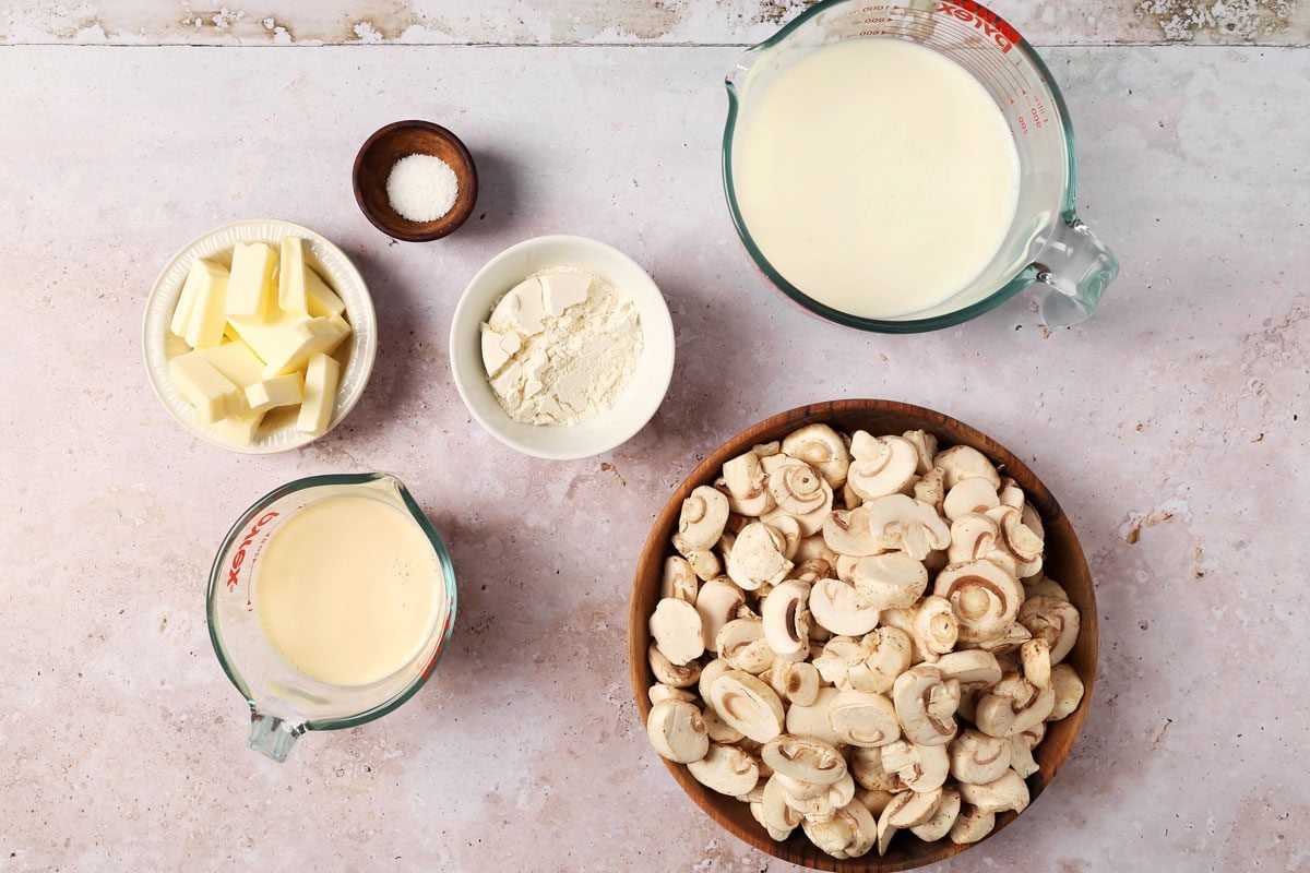 Ingredients for Taste of Home's Creamed Mushrooms laid out in small bowls on a grey surface.