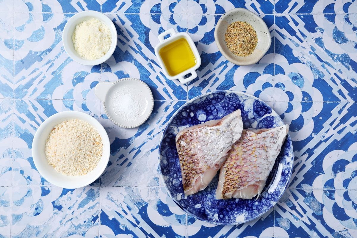 Close up of Taste of Home's Pan-Seared Red Snapper on a blue plate with peas and lemon slices on a blue and white tiled background.
