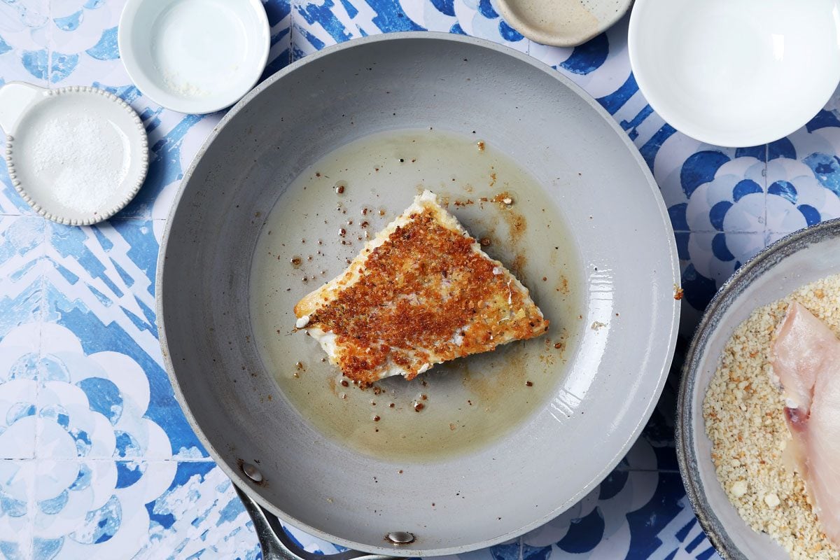 Process of making Taste of Home's Pan-Seared Red Snapper laid seared in a pan on a blue and white tiled background.